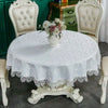 A round white lace tablecloth with an elegant embroidered edge set on a dining table surrounded by antique chairs.