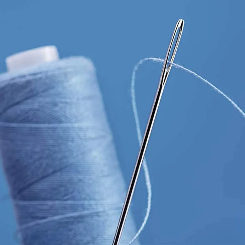 A close-up of a stainless steel hand sewing needle with white thread next to a blue spool of thread.
