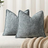Two gray chenille throw pillows resting on a light surface next to a beige knitted blanket.