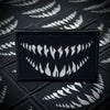 A black tactical hook and loop emblem patch is displayed against a dark background with repeating white tooth patterns.