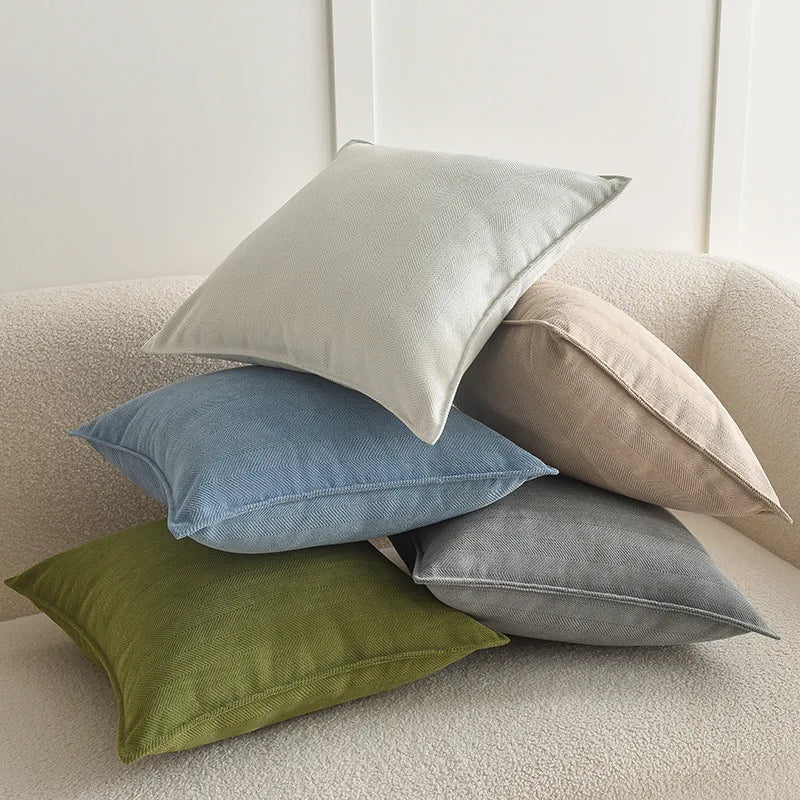A collection of various colored throw pillows, including gray, blue, beige, and olive green, resting on a light-colored sofa.