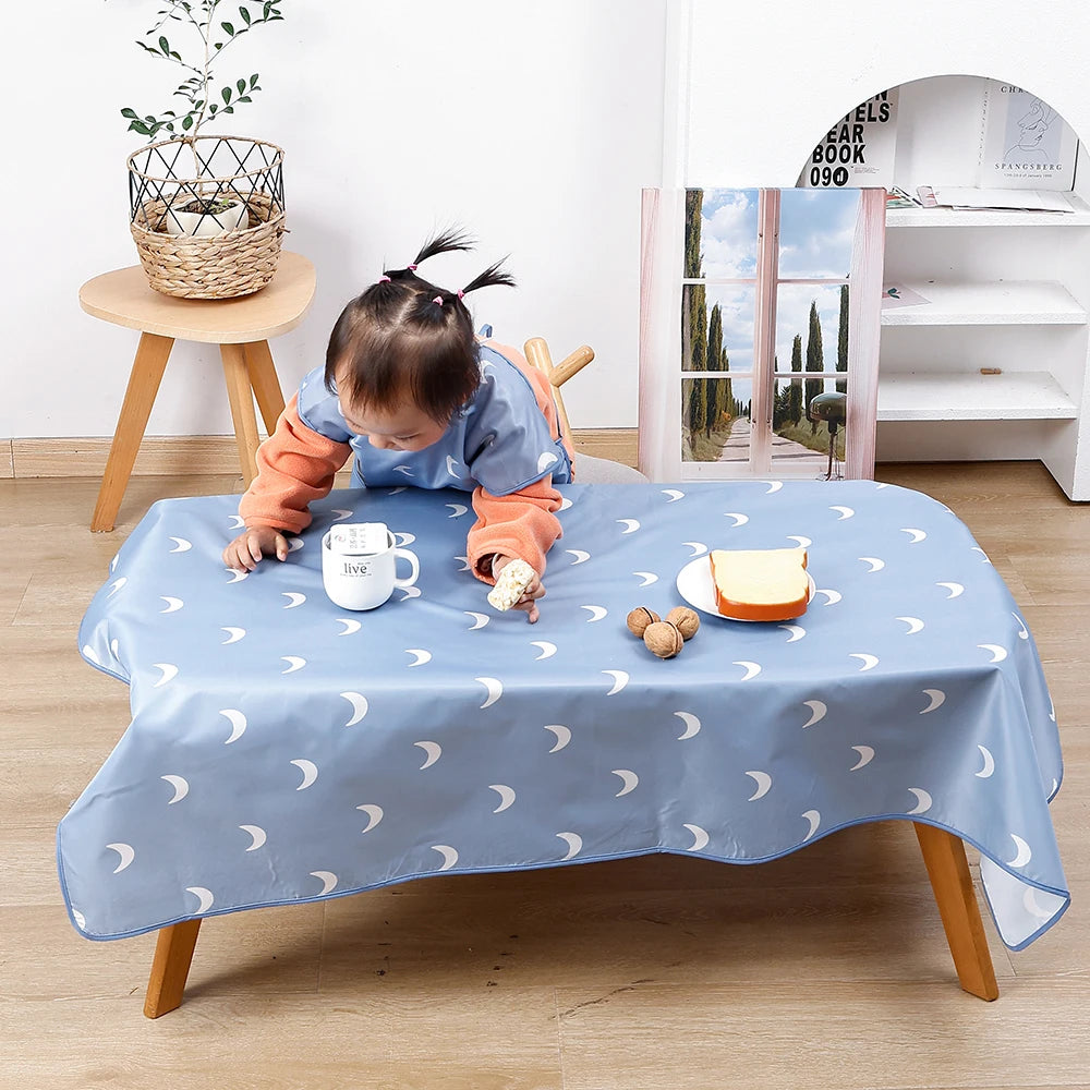 A light blue waterproof baby play mat with anti-slip backing is laid out on a wooden table.