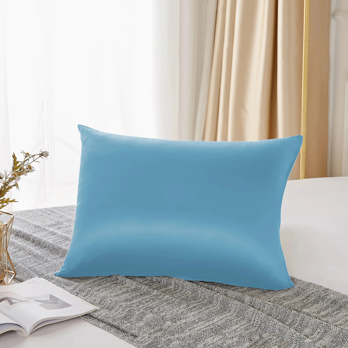 A light blue pure mulberry silk pillowcase resting on a gray textured fabric.