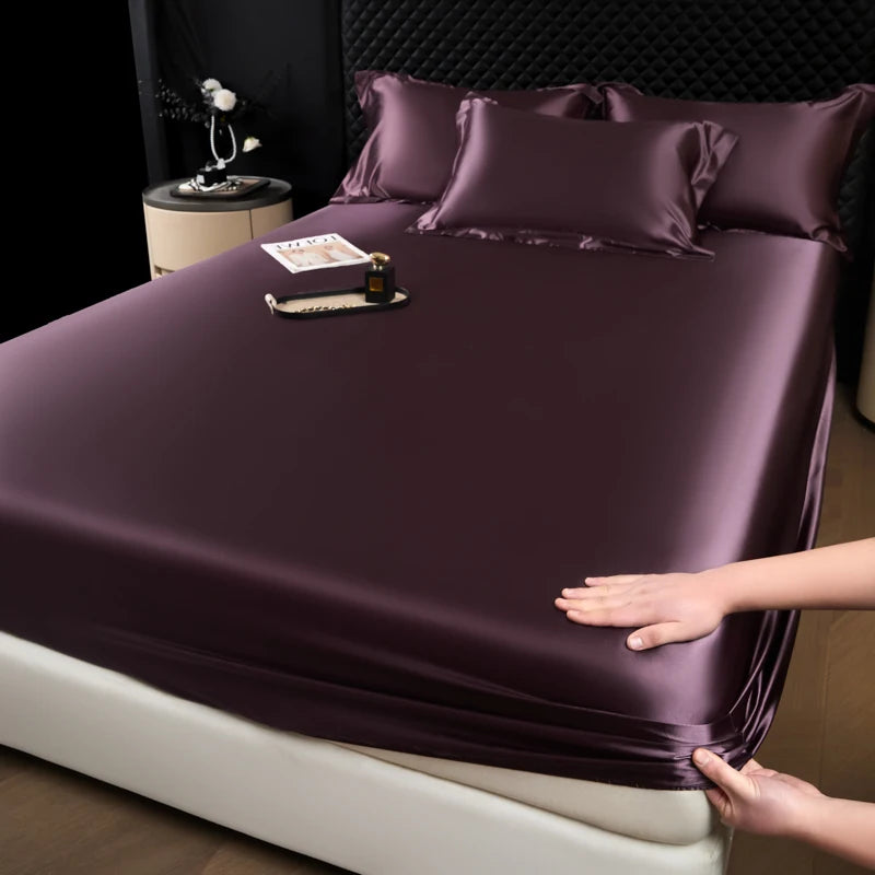 A close-up of a deep purple satin fitted sheet covering a mattress, with a hand touching the fabric.