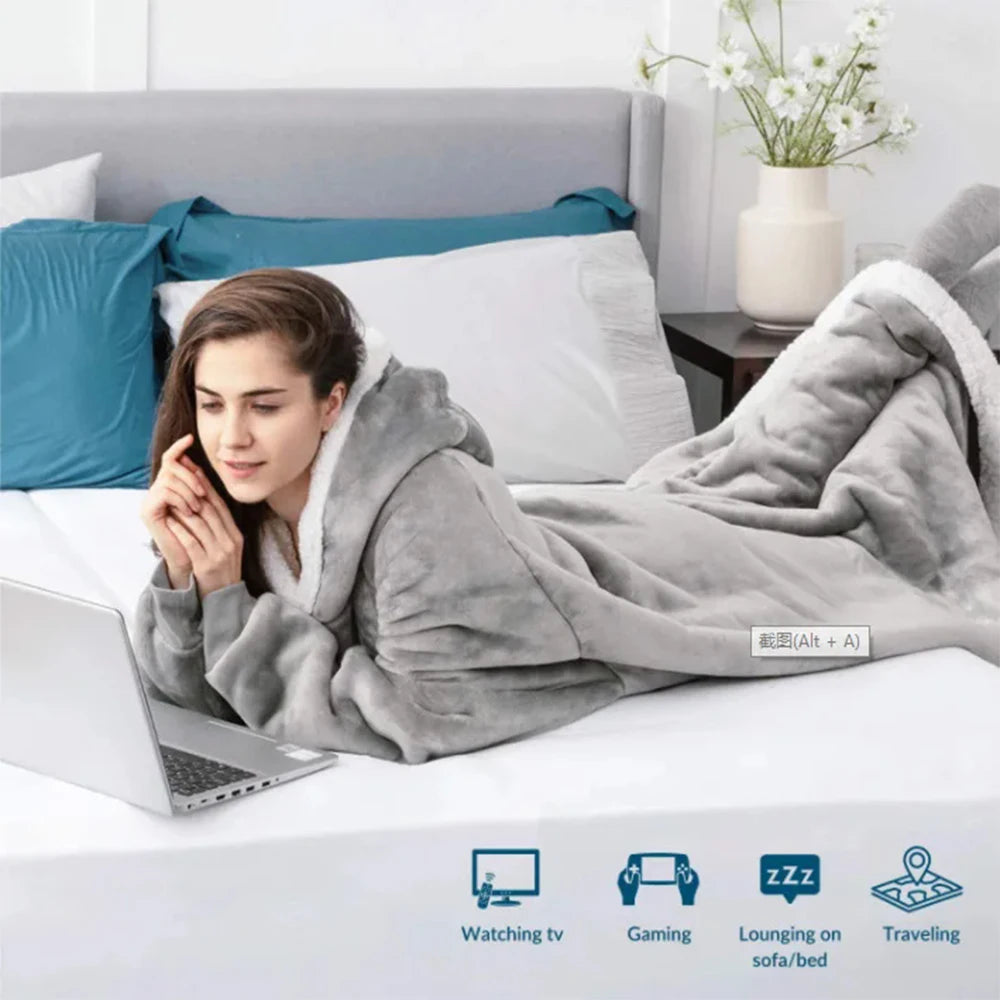 A woman is relaxing on a bed with a gray flannel blanket and a laptop.