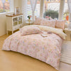 A pink floral duvet cover and pillow set displayed on a bed in a bright room with white curtains.