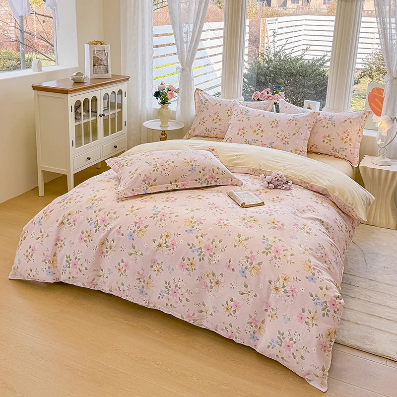 A pink floral duvet cover and pillow set displayed on a bed in a bright room with white curtains.