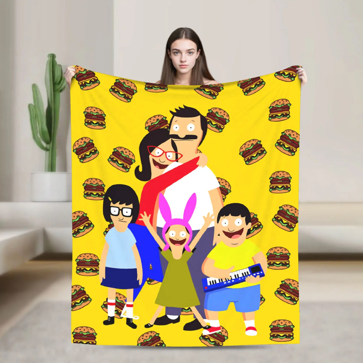 A woman holding a yellow throw blanket featuring characters from an anime or funny theme.