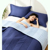 A woman is relaxing on a bed covered with a navy blue quilted blanket and pillows.