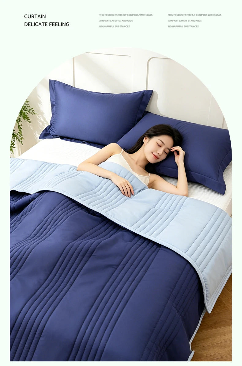 A woman is relaxing on a bed covered with a navy blue quilted blanket and pillows.