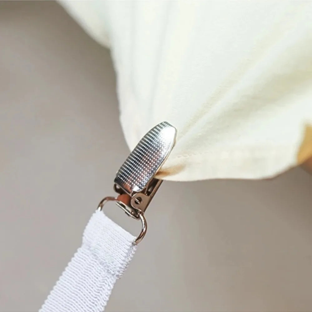 A close-up of a silver bed sheet clip attached to a white strap, used for securing bedding.