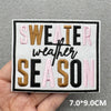 Black and pink embroidered text on a white patch that reads SWEATER WEATHER SEASON