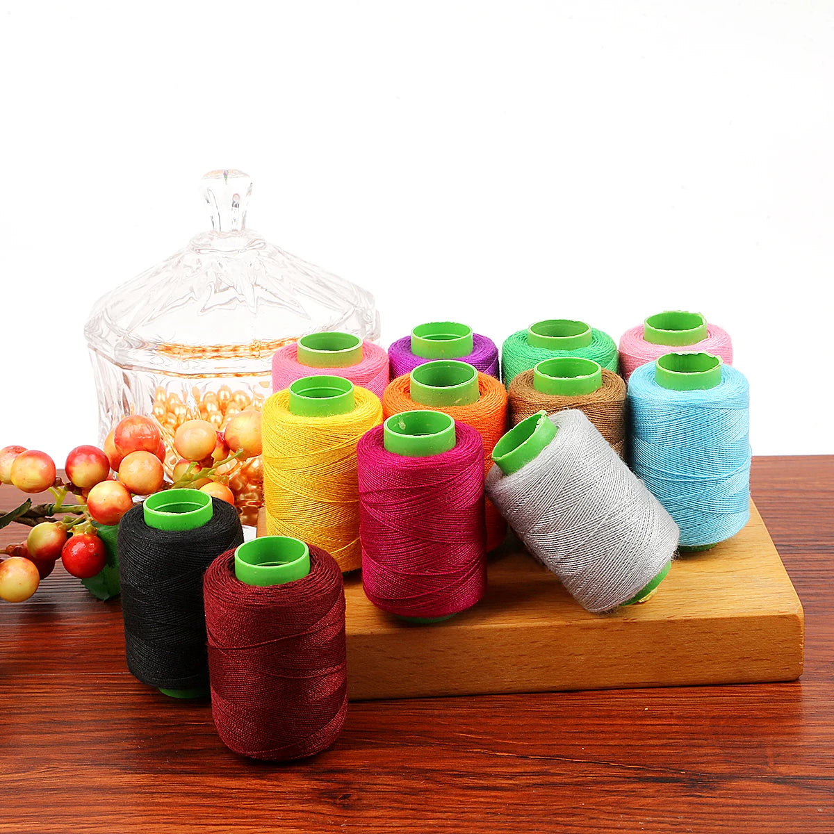 A collection of 24 spools of colored sewing threads in various shades of green, pink, yellow, and blue resting on a wooden bo