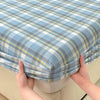 A close-up of a light blue and gray plaid fitted sheet being held by hands.
