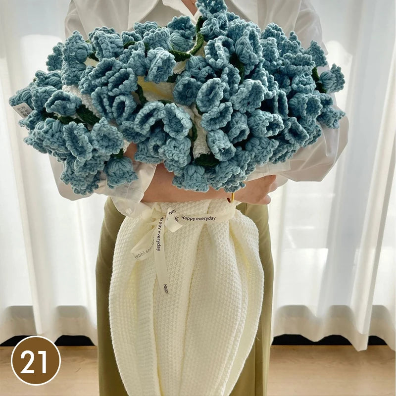A hand knitted floral rose bouquet is held against a cream colored throw blanket.