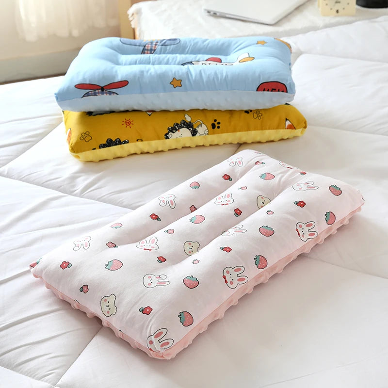 Two stacked reversible cartoon animal fiber pillows in blue and yellow resting on white bedding.