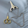 Vintage stainless steel sewing scissors and a decorative metal charm displayed on a gray background.