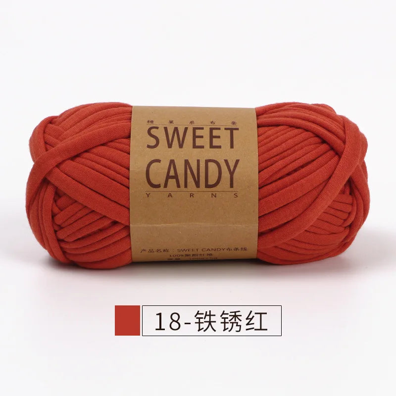 A skein of orange-red yarn labeled Sweet Candy Yarns, tightly wound and displayed on a white background.