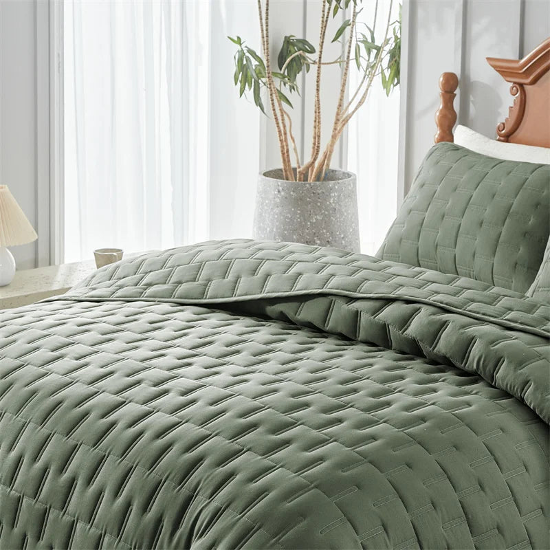 A close-up of a sage green quilted duvet and pillow set on a bed, with a potted plant in the background.