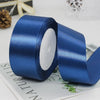 A roll of deep blue satin craft ribbon with white filling, lying on a white surface.
