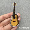 An embroidered patch of a brown acoustic guitar with a yellow body and white pickguard, shown being held by a hand.