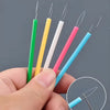 A hand holds several colorful needle threaders with sharp points against a gray background.