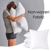 A woman is hugging a large white pillow against a gray wall, with another white cushion visible in the foreground.