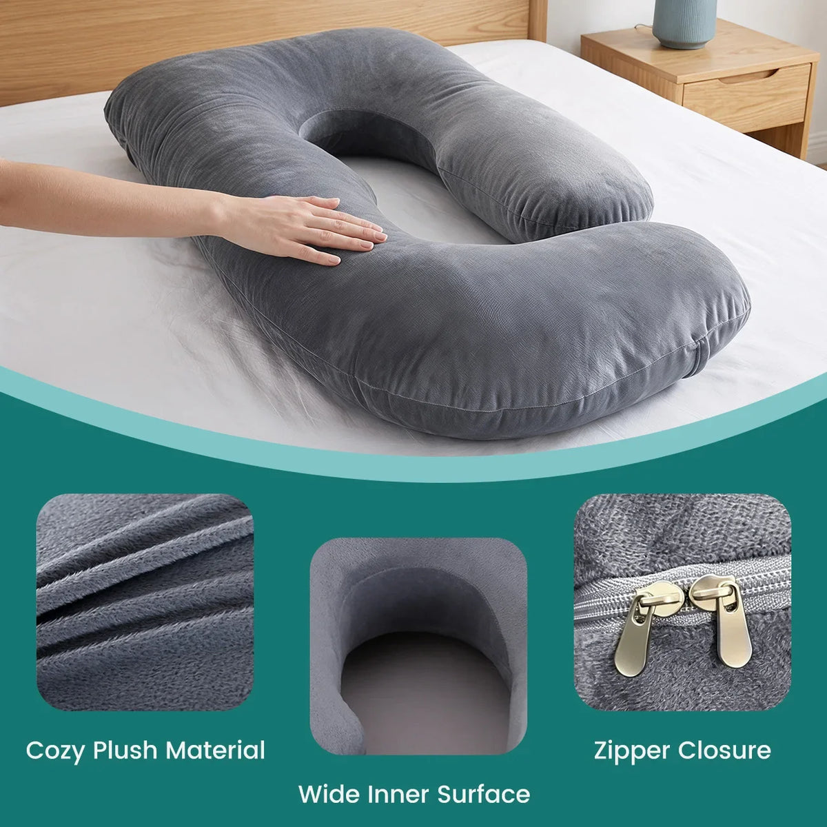 A gray ergonomic J-shaped maternity pillow with a zipper closure and wide inner surface resting on a white bed.