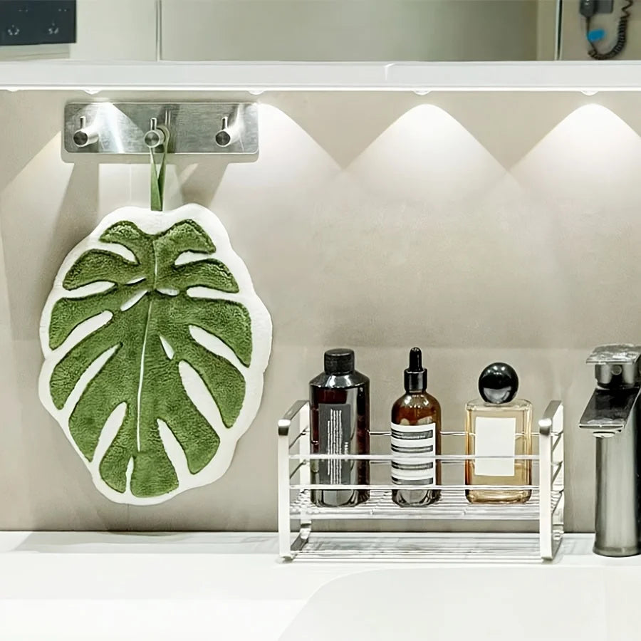 A white leaf-shaped hand towel is hanging on a silver hook above a counter with various glass bottles.