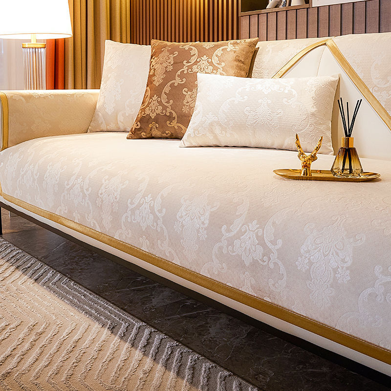 A beige luxury velvet sofa cover with decorative pillows and gold accents in a modern interior setting.