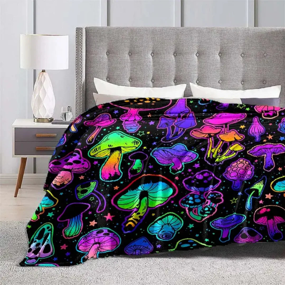 A colorful mushroom flannel throw blanket displayed on a bed with a white lamp and gray headboard.