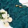 A deep teal fabric draped with ruffled folds, featuring gold-toned decorative spoons and white flowers.