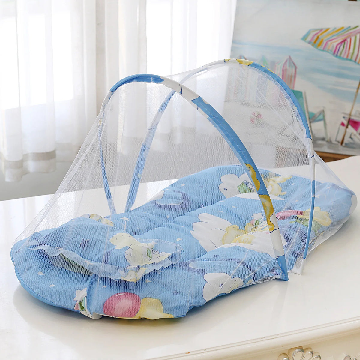 A light blue foldable baby mosquito net sleeping tent with a floral pattern is displayed on a white surface.