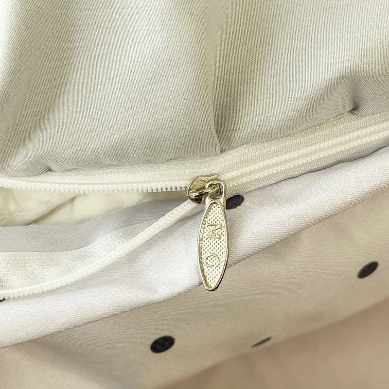 Close-up of a satin duvet cover zipper with a gold-toned logo tag on a light beige fabric.