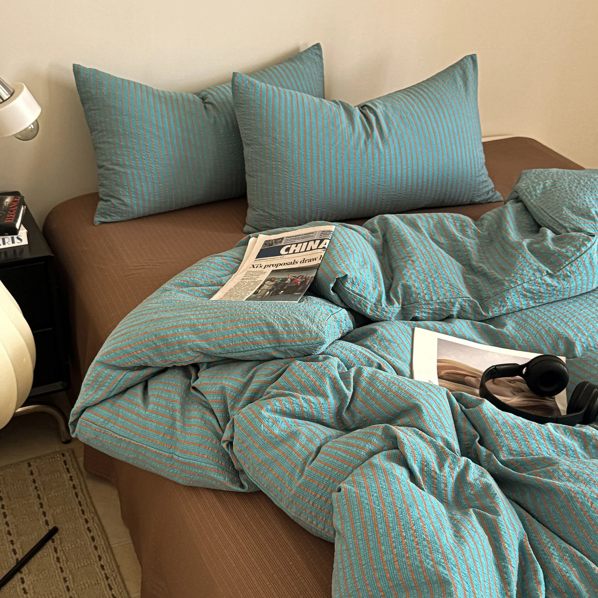 A teal striped duvet cover set with matching pillows is displayed on a bed.