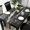 A black dining table set with a modern abstract marble linen table runner featuring gold veins and white plates.