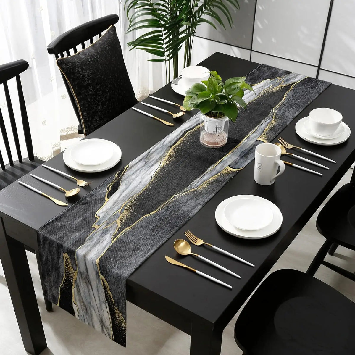 A black dining table set with a modern abstract marble linen table runner featuring gold veins and white plates.