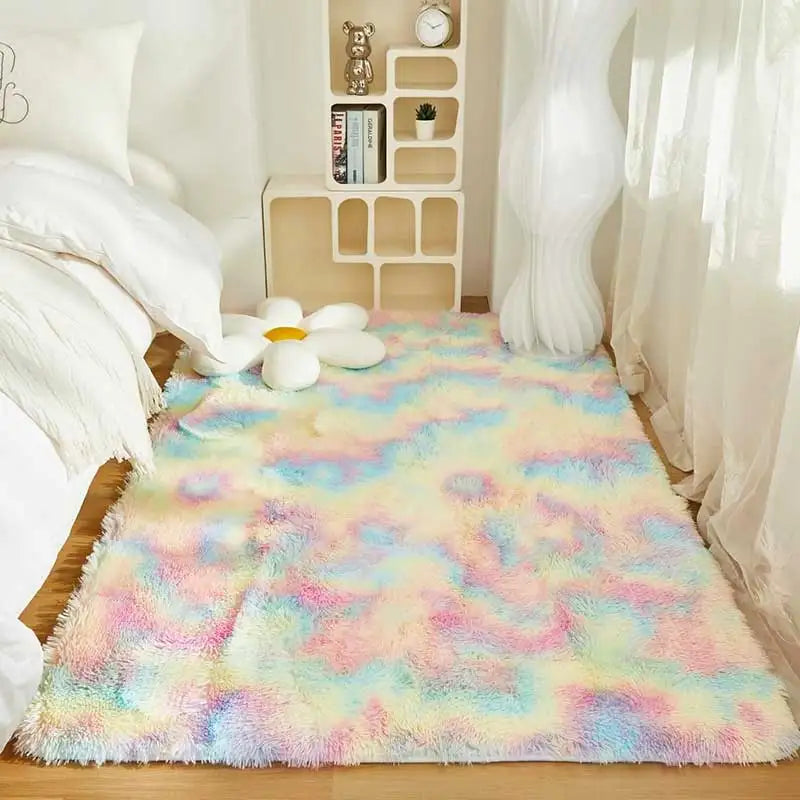 A fluffy rainbow colored plush area rug laid out on a wooden floor next to a white bed and shelving unit.