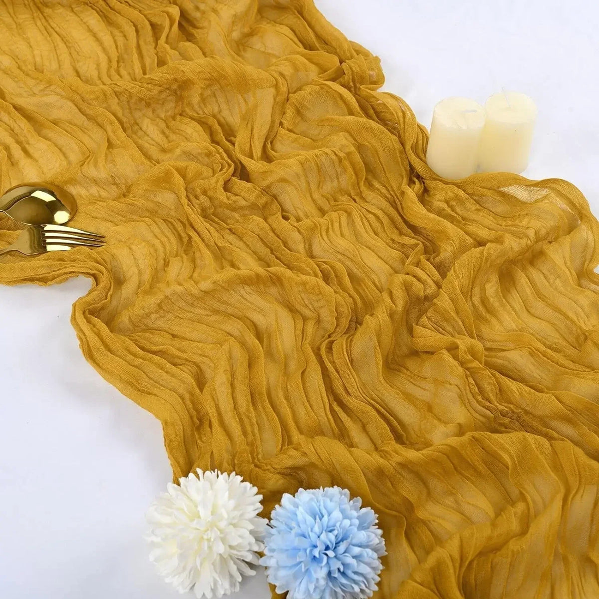 A golden yellow rustic gauze table runner draped with white candles and floral accents.