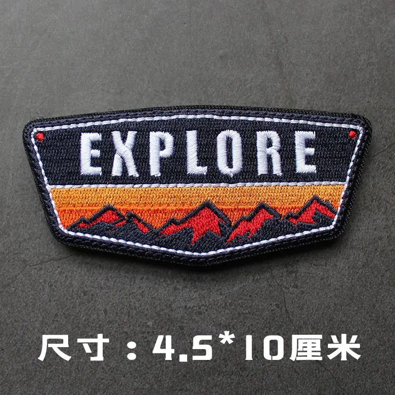 Black embroidered badge with the word EXPLORE in white and orange text on a dark gray background