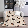 A beige flannel blanket featuring a pattern of black and tan dachshund silhouettes on a light gray sofa.