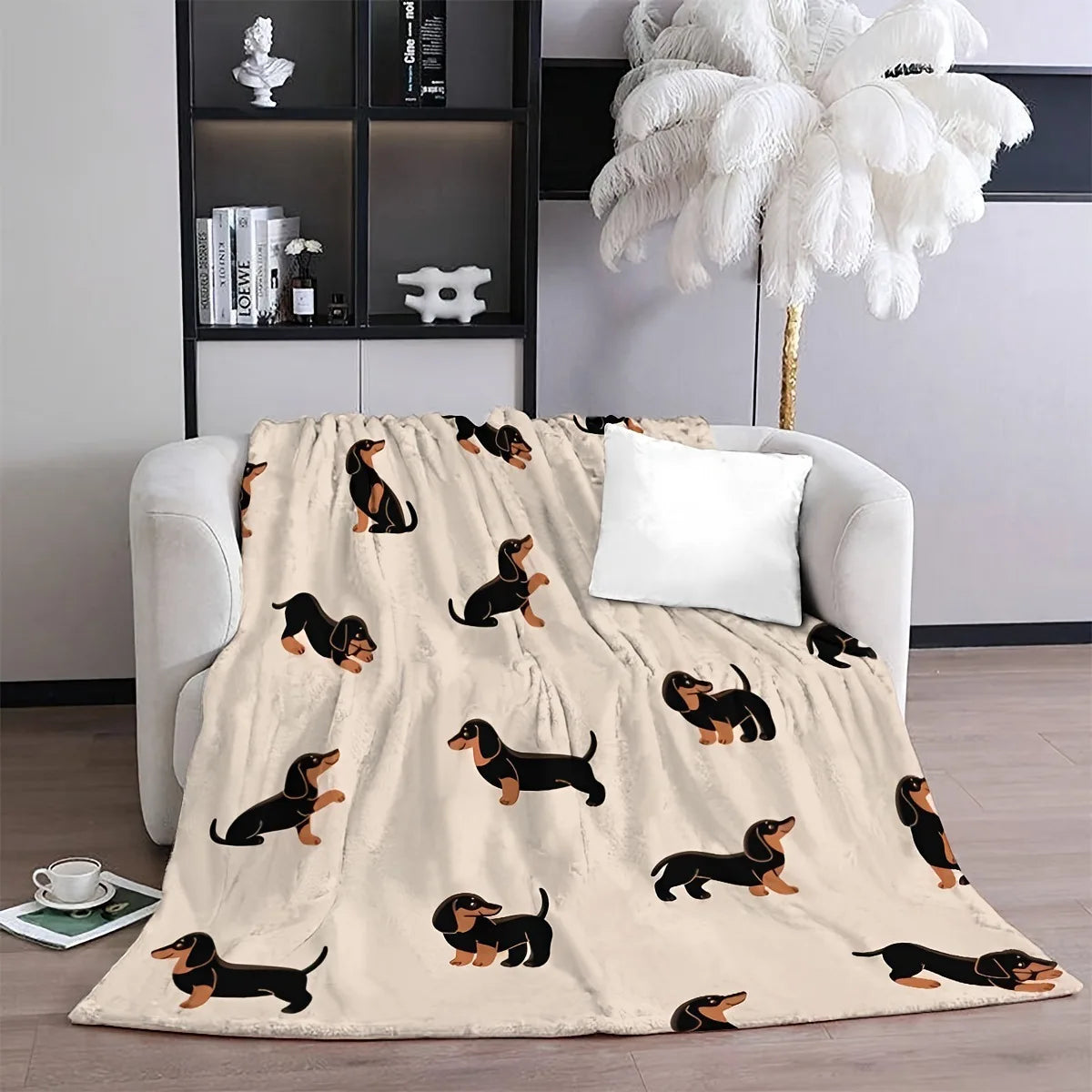 A beige flannel blanket featuring a pattern of black and tan dachshund silhouettes on a light gray sofa.