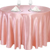 A round table set with a pink satin overlay cloth, glassware, and silverware.