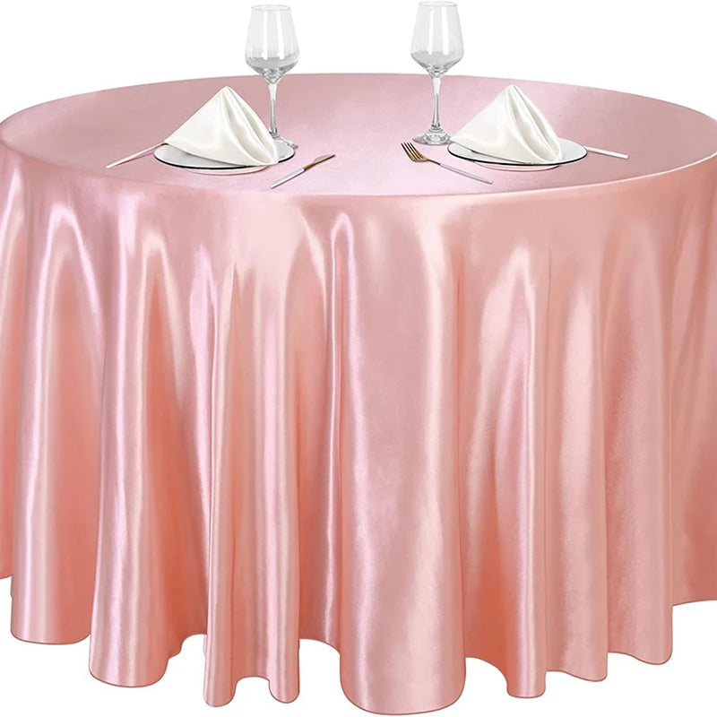 A round table set with a pink satin overlay cloth, glassware, and silverware.