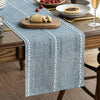 A blue embroidered cotton linen table runner with white tassels placed on a wooden table.