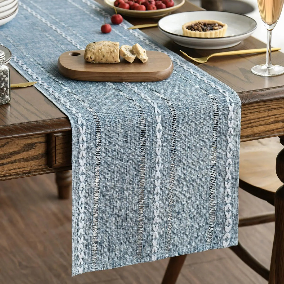 A blue embroidered cotton linen table runner with white tassels placed on a wooden table.