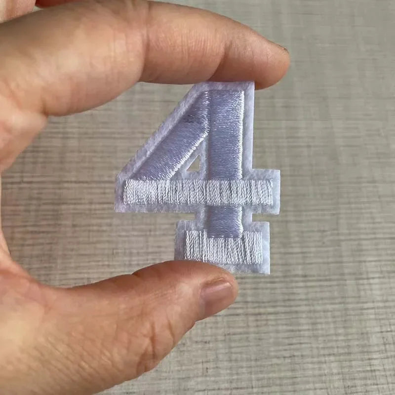 A hand holds a light purple embroidered number four patch.