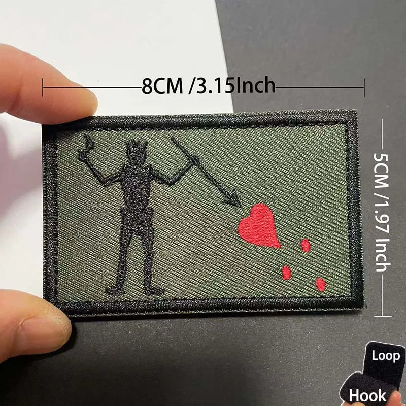 An embroidered patch depicting a silhouette of a pirate figure and a red heart with blood splatters on a dark green fabric.
