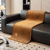 A brown quilted sofa cover draped over a black leather sofa in a modern living room setting.