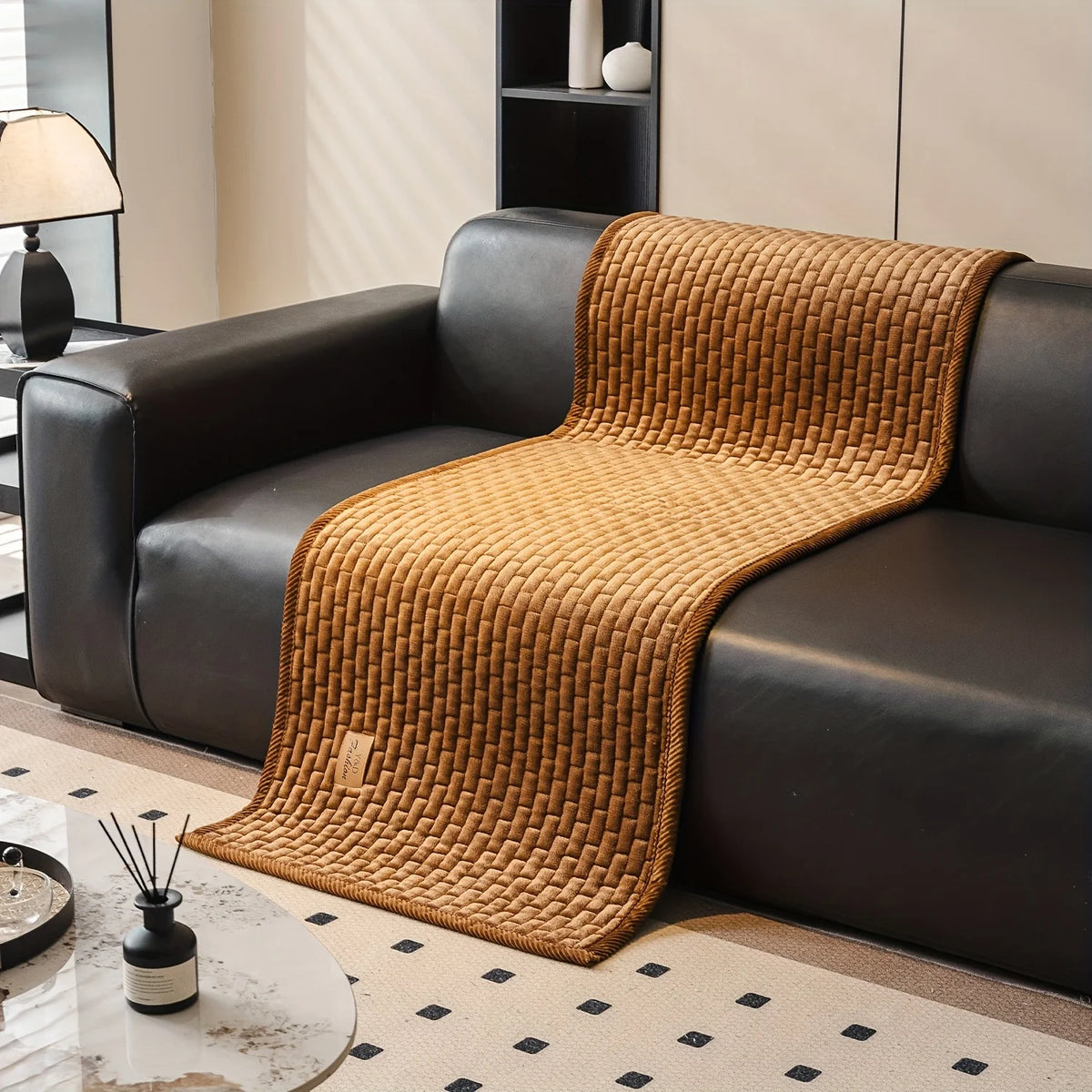 A brown quilted sofa cover draped over a black leather sofa in a modern living room setting.